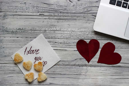 Background of a valentine on a wooden table with a laptop cookies in the form of hearts beside a napkin for inscription. Valentine's Day.の写真素材