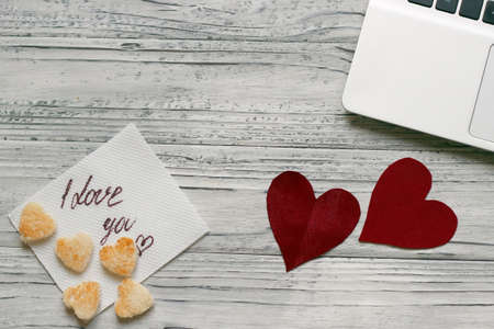 Background of a valentine on a wooden table with a laptop cookies in the form of hearts beside a napkin for inscription. Valentine's Day.の写真素材