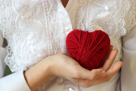 Children's hands hold a heart of red thread for knitting.の写真素材
