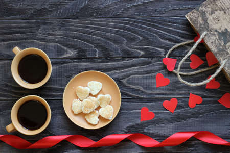 On a dark wooden background, there are two cups of coffee, red paper hearts and gifts for Valentine's Day.の写真素材