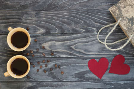On a dark wooden background, there are two cups of coffee, red paper hearts and gifts for Valentine's Day.の写真素材