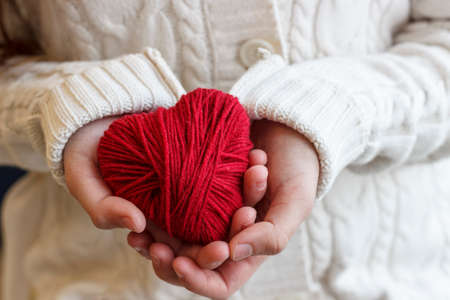 Children's hands hold a heart of red thread for knitting.の写真素材