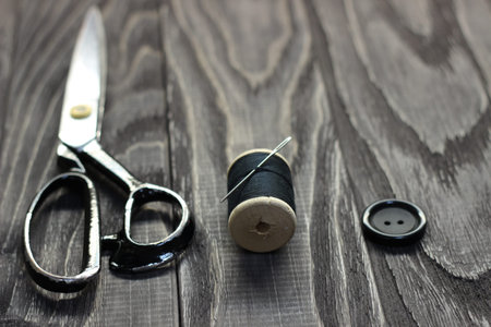 On a black wooden stench, close-up, scissors spool of thread with a needle.