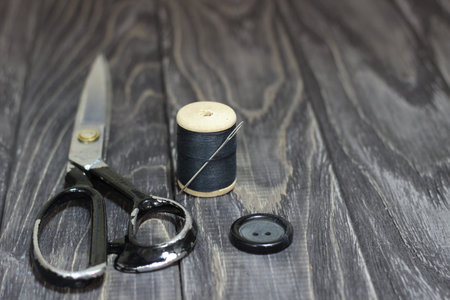 On a black wooden stench, close-up, scissors spool of thread with a needle.