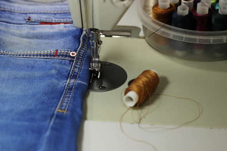 On the table of the sewing machine lie denim fabrics, close-up, next to the thread and scissors.の写真素材
