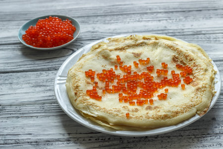 Pancakes with red caviar in a white plate on a wooden background. Celebration of Maslenitsa