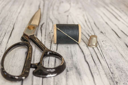 On a white wooden background is a spool of thread with a needle scissors and a place for text.の写真素材
