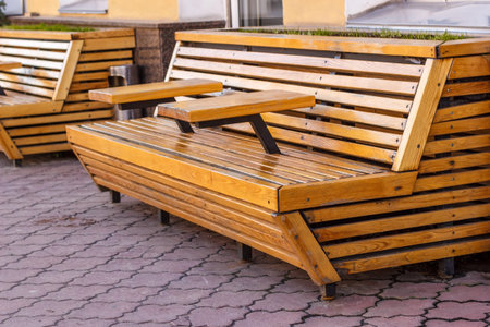 A wooden bench with tables on a stone pavement.