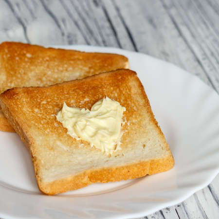Still life with bread and butter in a white plate on a wooden backgroundの写真素材