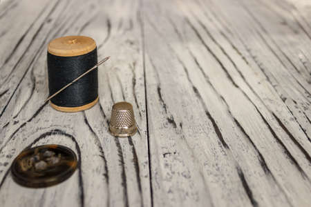 On a white wooden background is a spool of thread with a needle and a place for text.の写真素材