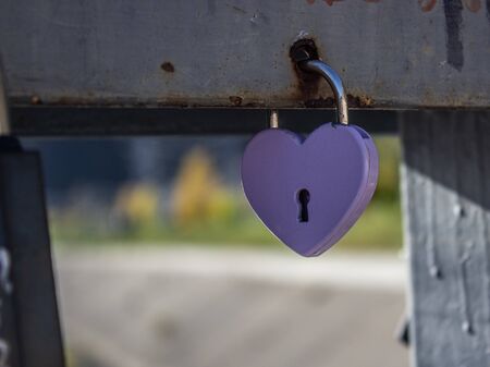 A gold padlock in a heart form hanging on a steel rope of the bridge railing on the background of a river and another bridge. Photo 3の写真素材