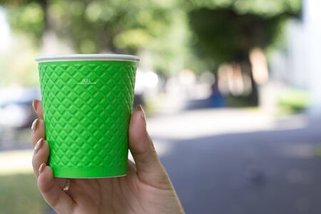 Mock up of cup coffee in woman's hand bright background for break, energy and strength, hot drink in paper cup. Tea or lemonade with ice, drink for business womanの写真素材