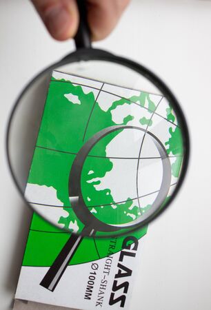 A hand with a magnifying glass examines objectsの写真素材