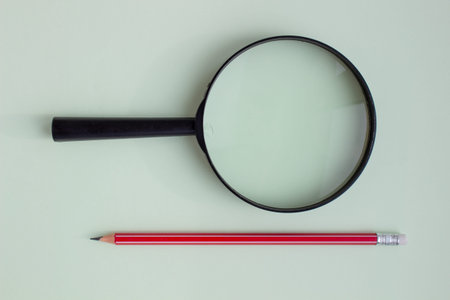One red pencil under a magnifying glass close-up on a light background