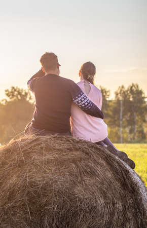 A young boy and a girl sit on a bale of hay and enjoy a happy life in the country.の写真素材