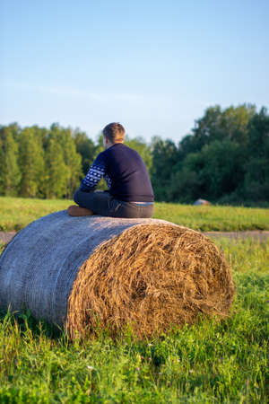 a Young boy sits on a hay bale and enjoys living happy on the country.の写真素材