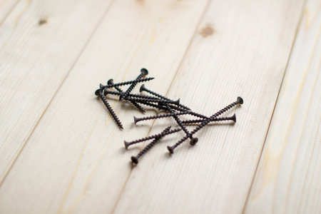 Black large screws or self-tapping screws made of high-strength steel for wooden products lie on a...