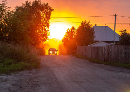 Beautiful sunset on the dusty street in front of the sun. Pink and orange sunset in the countrysideの写真素材