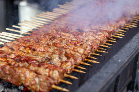 A lot of kebabs in a row on the grill. Kebabs strung on wooden skewers in a street cafe. The process of cooking kebabs with a lot of smoke.の写真素材