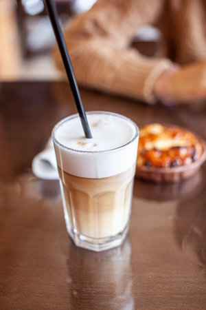 Hot Latte coffee in a glass and a fresh apple dessert next to it. The hot drink is served with a plastic straw. Delicious breakfast in the cafeの写真素材