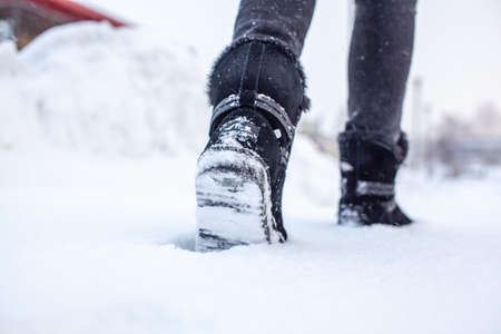 A person is walking on a slippery road, the first snow in the park, winter shoes, the road is covered with slippery ice and white snow. Footprints and shoes close-up.の写真素材