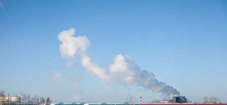 White thick smoke from the boiler room chimney. Smoke against the blue sky. Air pollution. Heating of the city. Industrial zone.の写真素材