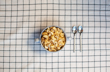 A plate of cashew nuts on a nice napkin and two spoons next to it.