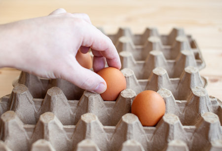 A man takes a brown egg from a cardboard bag with his hand, a chicken egg in his hand for cooking, a...