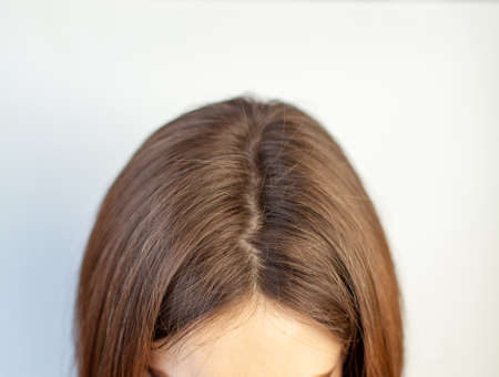A woman's head with a parting of gray hair that has grown roots due to quarantine. Brown hair on a woman's head close-up.の写真素材