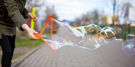 A girl blows soap bubbles in the park for the entertainment of children. Large, colorful soap...