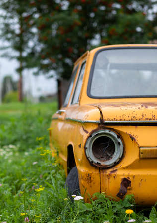 Old yellow wrecked car in vintage style. Abandoned rusty yellow car. Close-up of the headlights of the front view of a rusty, broken, abandoned car near the house. Concept of abandoned used car.の写真素材