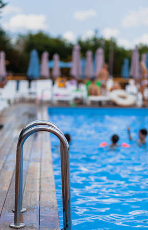 Ladder stainless handrails for descent into swimming pool. Swimming pool with handrail. Ladder of a swimming pool. People swim and relax in the poolの写真素材