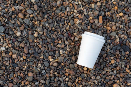 A white paper cup of coffee or tea lies on the rocky shore. A mug of hot drink on a pebble. Beautiful rocky background. free copy space.の写真素材