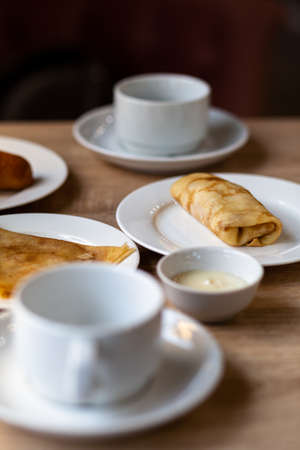 Fresh pancakes with filling on the table next to white mugs for coffee or tea for breakfast. Pancakes for a sweet dessert after lunch in a cozy coffee.の写真素材