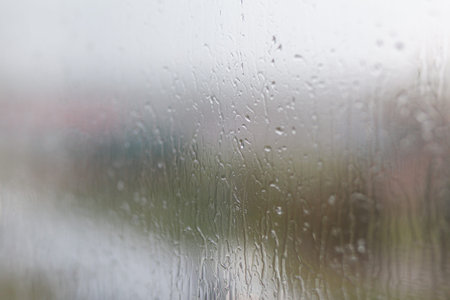 Rainy day through the window on cloudy grey sky and city buildings background. Concept. Evening cityscape behind the glass window with trickling drops of water.の写真素材