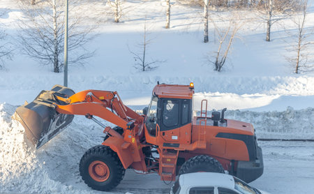 Big orange tractor cleans up snow from the road and loads it into the truck. Cleaning and cleaning...