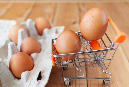 A few chicken eggs in the shopping basket next to cardboard bag, a chicken egg as a valuable nutritious product, a tray for carrying and storing fragile eggs. package of eggs, an important food itemの写真素材