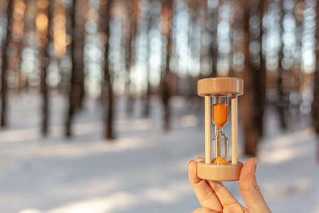 Winter is coming. Hourglass in the snow. sandglass Hourglass as a symbol of the changing of the seasons. Spring is coming. melting snow. Hourglass in a woman's hand in a snowy forest in winterの写真素材