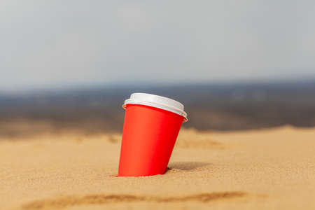 A red cup of coffee or a hot drink covered with a lid in the sand in the desert. sandy seashore.の写真素材