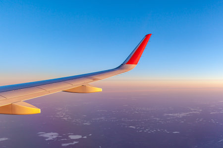Airplane flight at sunset or dawn. Aircraft's wing and land seen through the illuminator. View from...