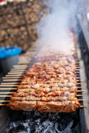 A lot of juicy meat kebabs in a row on the grill. Meat pieces strung on wooden skewers on the grill. The process of cooking kebabs with a lot of smoke. Cooking in natureの写真素材