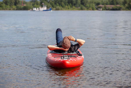 SUP board Stand up paddle man boarding on lake standing happy on blue water. A man swims and rests on a SUP board on the riverの写真素材