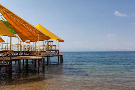 Swimming area or pier on the sea. A large pier with a roof, wooden planks and rusty stairs descending into the water. bathing and resting place.の写真素材