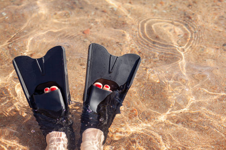 A woman in black flippers splashes near the shore. Fins stick out of the water. swimming equipment. Summer holidays, fun, exploring the sea world concept. Space for copy.の写真素材