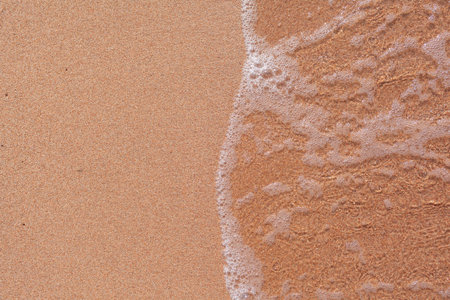 A soft wave runs on a sandy shore on a summer day. Empty space can be used as background for display...