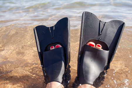 A woman in black flippers splashes near the shore. Fins stick out of the water. swimming equipment....