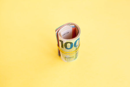 Money roll of euro banknotes yellow rubber band on yellow background