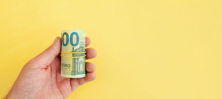 Money roll of euro banknotes yellow rubber band on yellow background
