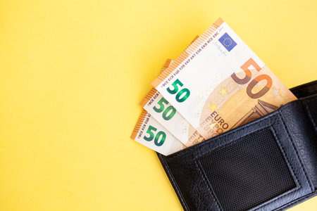 Fifty euro banknotes inside a black wallet on yellow backgroundの写真素材