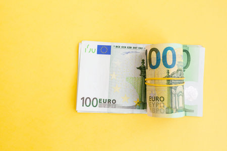 Money roll of euro banknotes with a elastic band on a 100 euro paper bill on a yellow background....